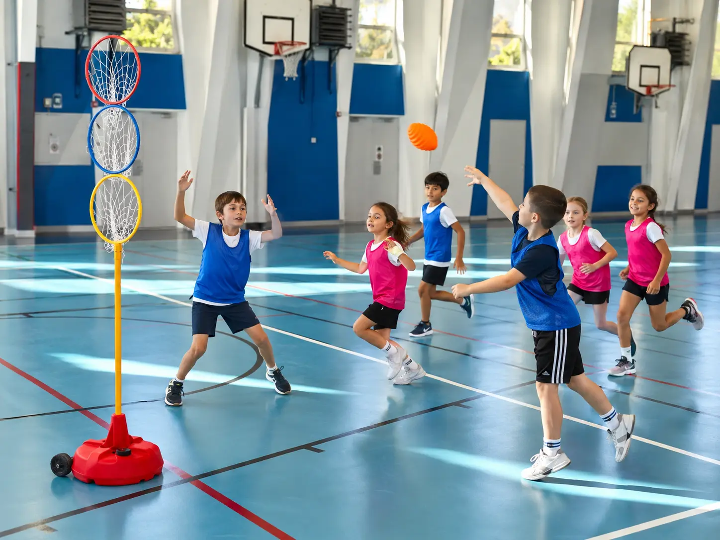 Enfants jouant au Cardiogoal en gymnase avec une cible à trois anneaux et un ballon spiralé orange.